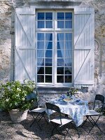 Gedeckter Gartentisch vor einem Sprossenfenster mit Fensterläden