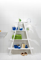 Blue and green accessories on white ladder shelves in bathroom