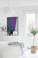 Small olive tree planted in basket and boldly coloured artwork in white bedroom