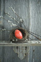 Hand-painted red Easter egg in willow nest and branches of pussy willow on wooden shelf