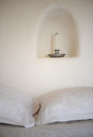Candle in candle holder in small niche above bed