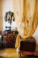 Artistically draped curtains in front of designer jacket on wall above vintage sewing machine on chest of drawers