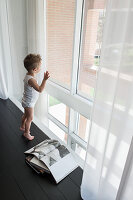 Little boy standing on black floor next to window