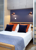 Double bed with reading lamps on purple wall and wall-mounted cupboards