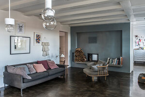 Cosy chair and sofa on concrete floor in front of fireplace with blue wall