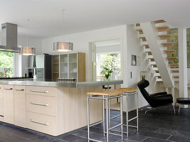 Kitchen island with a light front and stainless steel worktop, bar stool, and designer chair
