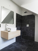 Simple vanity under the mirror in a white bathroom with anthracite-colored tiles