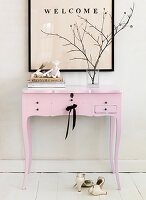 A picture with writing above a pink console table