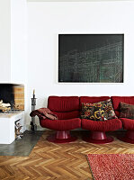 Red retro sofa under the black picture next to the fireplace