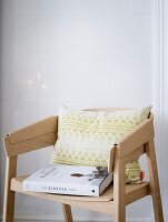 Gemustertes Kissen und Wohn-Buch auf modernem Stuhl