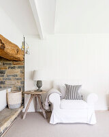 Loose-covered armchair and side table next to rustic niche in converted barn