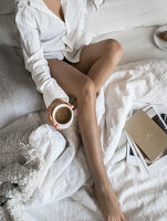 Frau im Pyjama mit einem Becher Kaffee auf dem Bett