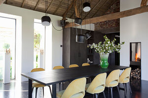 Yellow upholstered chairs around black table in dining room with exposed roof structure