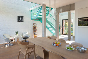 Bright dining room with wooden table and white brick wall, turquoise-colored staircase in the background