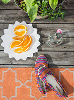 Orangenschnitze auf weißem Teller, Pflanze, Bügelflasche und bunte Schuhe auf Teppich
