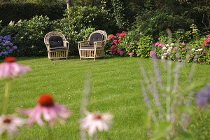 Rattan armchairs next to flower bed in garden