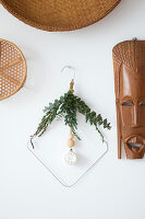 Bent metal coat hanger decorated with twigs on wall next to ethnic mask