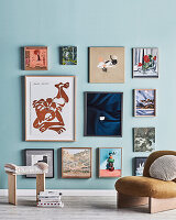 Gerahmte Bilder an hellblauer Wand, Hocker und Sessel davor