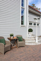 Rattan armchairs and table outside white wooden house