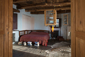 Double bed and zebra-skin rug in rustic bedroom with wood-beamed ceiling