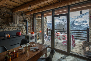 Kitchen and dining area in room with stone walls and wood-beamed ceiling: view of balcony and mountain landscape