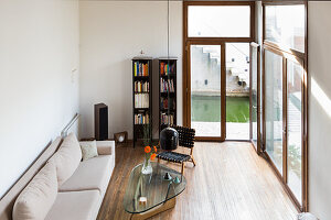 Pale couch, glass table and bookshelves next to French windows in living room