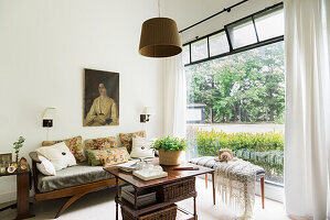 Sofa mit Kissen, darüber Frauenportrait, Tisch und Bank im Zimmer mit Gartenblick