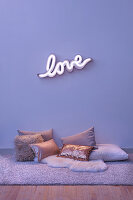 Neon wall light spelling 'LOVE' and various cushions on the floor