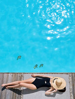 Woman wearing swimsuit lying by swimming pool with straw hat over face