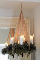 Hanging Christmas wreath with white candles and apricot colored decorative ribbon