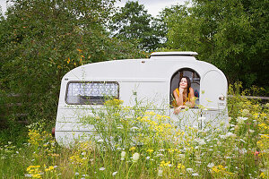 Young woman looking out of caravan in idyllic meadow