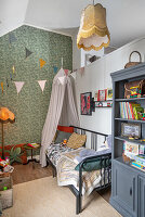 Regalschrank und Bett mit Baldachin im Kinderzimmer mit Tapete und hoher Decke
