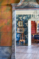 Blick durch Türrahmen mit Malerei auf alte Fotos und Stuhl vor Wand mit Tapete