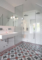 Glass enclosed shower area in a bathroom with white wall tiles and patterned floor tiles