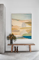 Vase on wooden bench below painting on wall of foyer