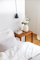 Bett, Nachttisch mit Blumen und Pendelleuchte vor weißem Raumteiler