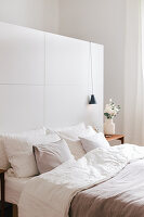 Bed, bedside table with flowers and pendant lamp in front of a white room divider