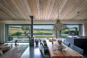 Wooden dining table in open-plan interior with sliding glass door and view of pool and countryside