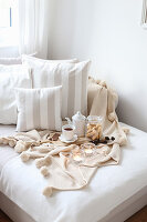Wooden board with tea, cookies and chocolate on bed