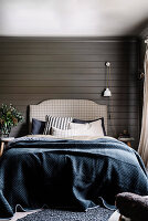 Double bed with pillow collection and blue bedspread in front of dark wall