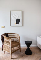Wicker chair and side table in hourglass shape below graphic artwork on wall