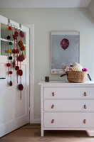 Garlands on door next to chest of drawers with loops as handles