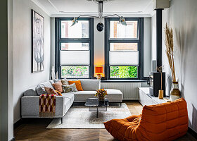 Grey corner sofa, coffee table, low sideboard with fireplace on top and orange two-seater in living room