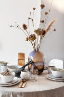 Table set with linen cloth, ceramic tableware, glass vase and dried grasses
