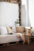 Gemütliches Sofa mit Kissen, Decke und Buch, dahinter Trockenstrauß aus Kugeldisteln auf der Terrasse