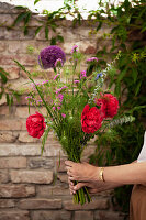 Woman holding an early summer bouquet of peonies, alliums, sea lavender, love-in-a-mist and eucalyptus