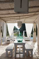 Ballonflasche auf Holzstisch und Bänke auf überdachter, mediterraner Terrasse