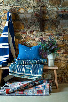 Bank mit Teppich, Kissen und Decke in Blautönen vor Natursteinwand