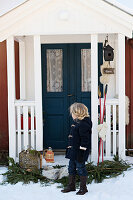 Child standing in front of a house entrance decorated for Christmas