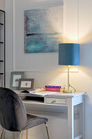 Grauer Polsterstuhl, Schreibtisch mit Tischlampe, darüber moderne Kunst